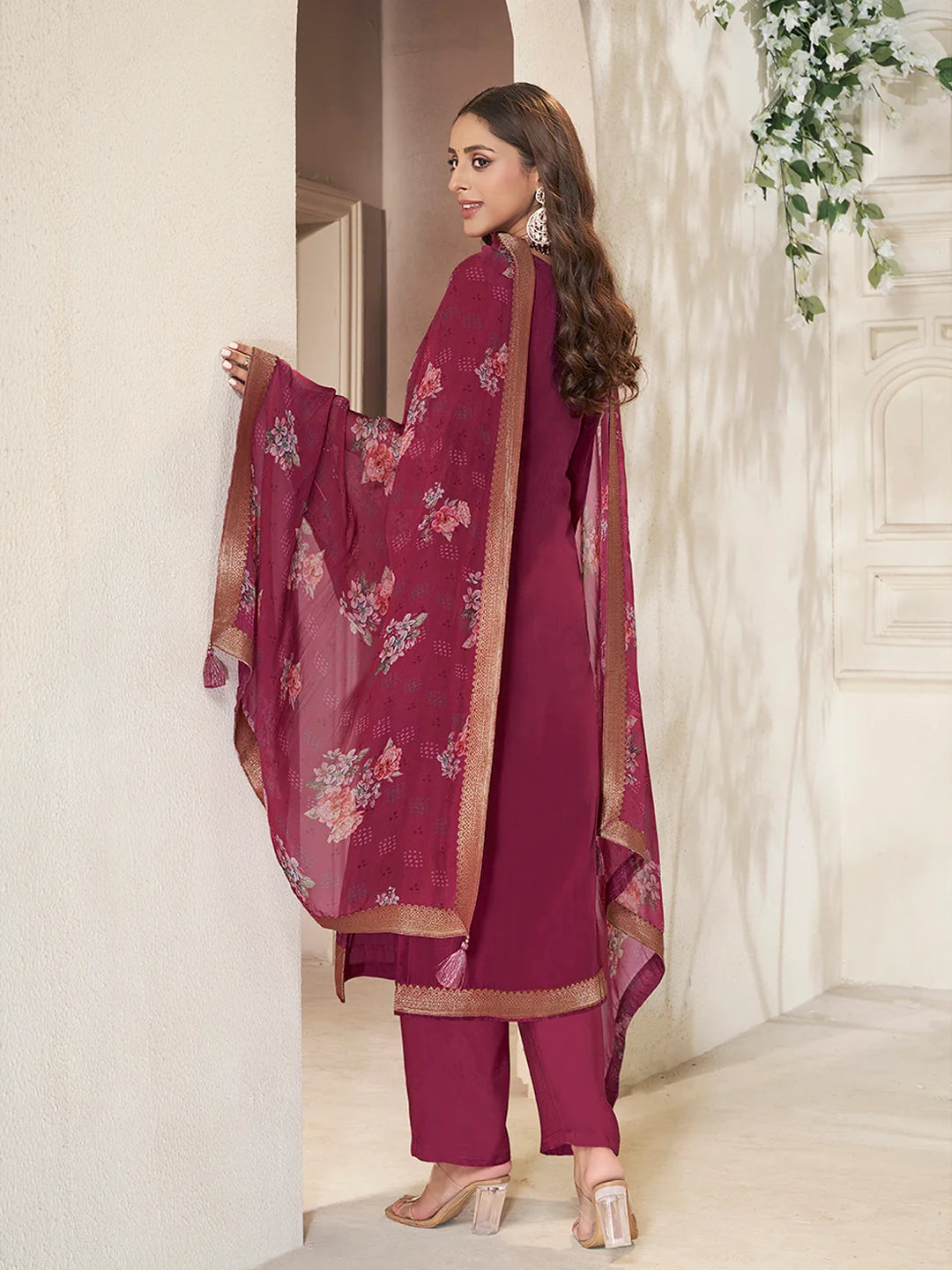 Woman in a maroon kurta set traditional outfit with floral patterns in a decorated room.