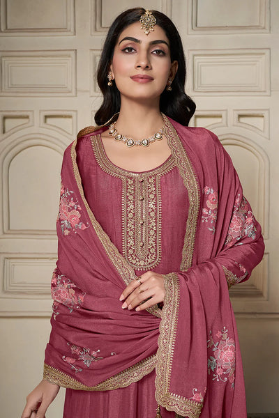 Woman wearing a traditional anarkali pink embroidered outfit with a matching dupatta against a beige wall.Woman wearing a traditional anarkali pink embroidered outfit with a matching dupatta against a beige wall.