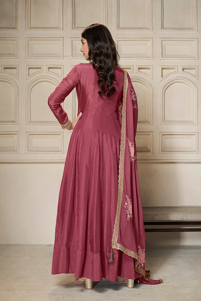 Woman wearing a pink traditional anarkali outfit with a matching dupatta against a neutral wall.Woman wearing a pink traditional anarkali outfit with a matching dupatta against a neutral wall.