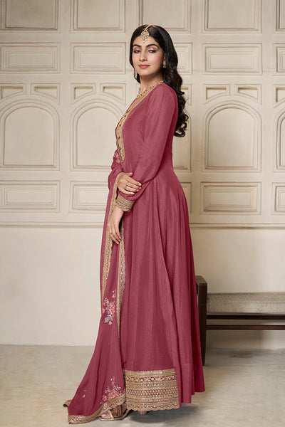 Woman in a traditional pink anarkali outfit with gold embroidery against a neutral wall.Woman in a traditional pink anarkali outfit with gold embroidery against a neutral wall.