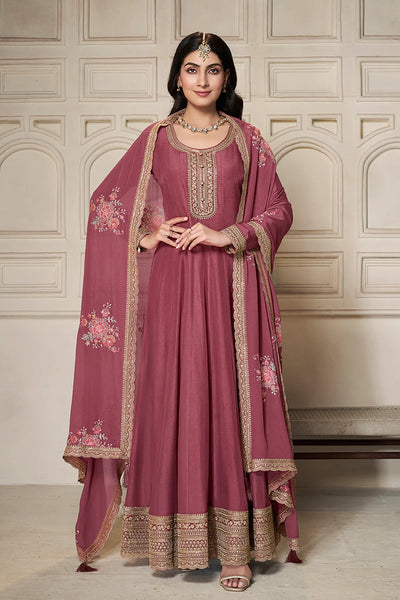 Woman wearing a traditional anarkali pink outfit with gold embroidery in an elegant setting.