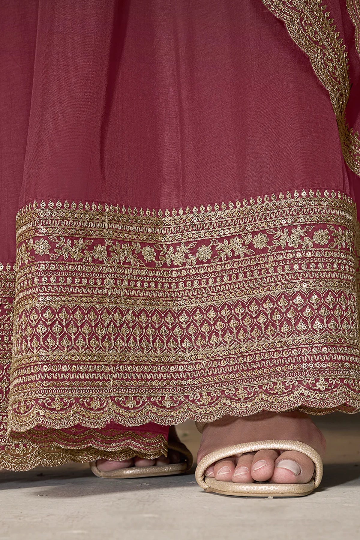 Close-up of a pink anarkali traditional outfit with gold embroidery and sandals on a neutral background