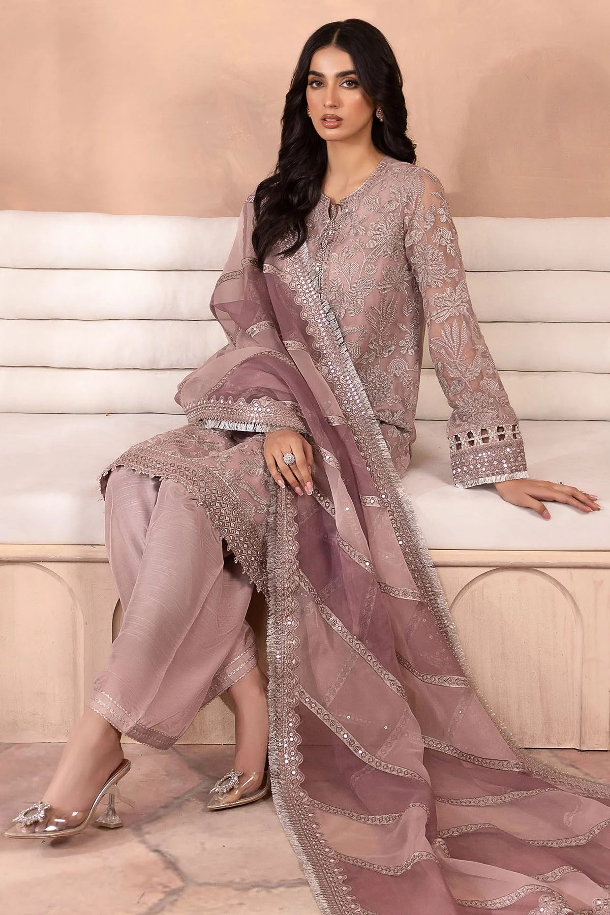 Woman in a traditional salwar suit outfit with intricate embroidery sitting on a white bench.