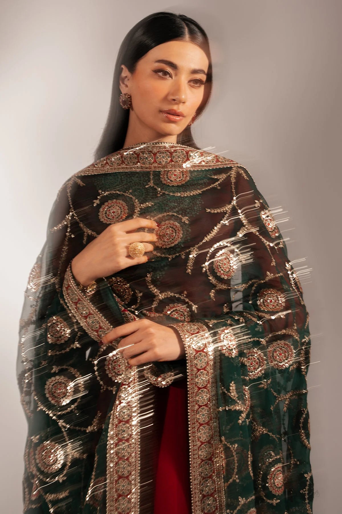 Woman wearing a traditional anarkali outfit with a maroon top and black dupatta with gold embroidery on a neutral background