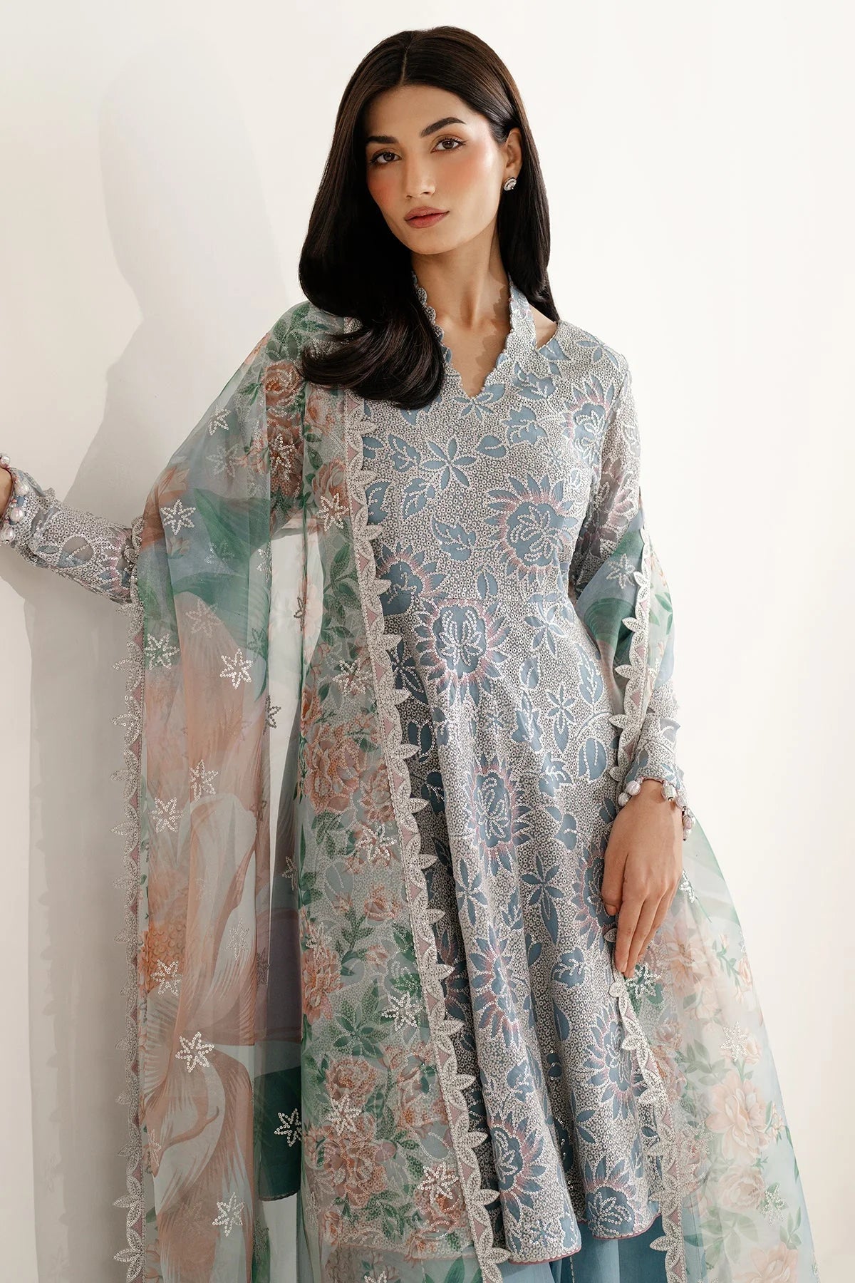 Woman wearing a traditional outfit with embroidered chiffon anarkali top and light blue palazzo pants on a plain background