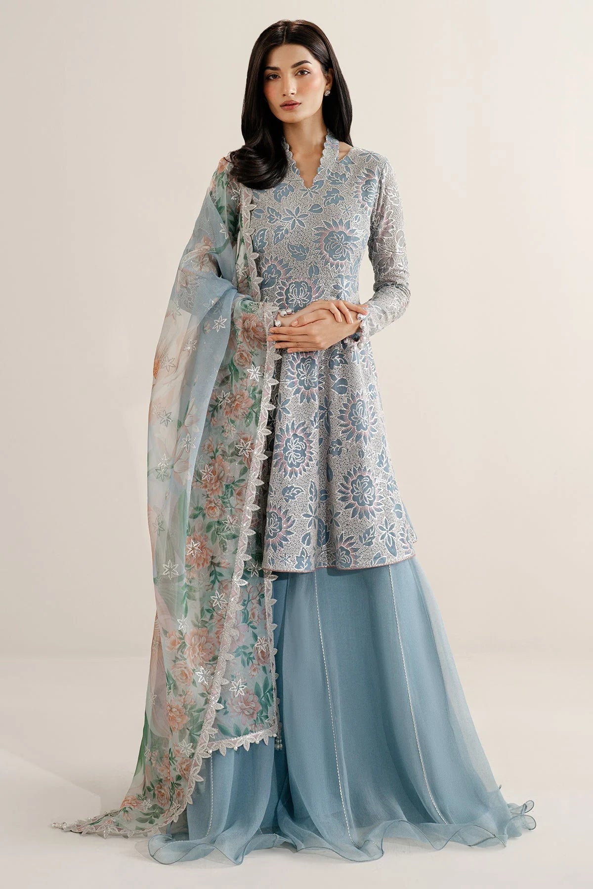 Woman wearing a traditional outfit with embroidered chiffon anarkali top and light blue palazzo pants on a plain background