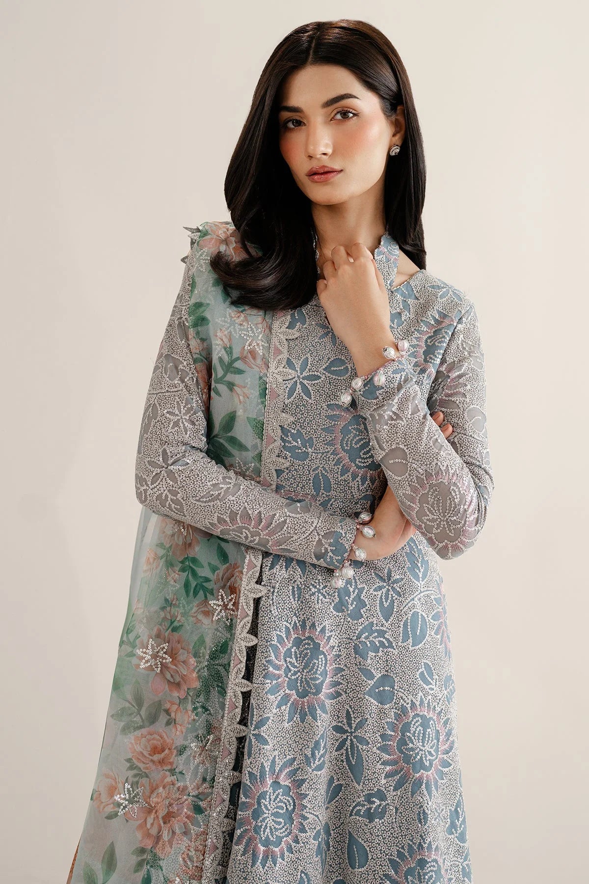 Woman wearing a traditional outfit with embroidered chiffon anarkali top and light blue palazzo pants on a plain background