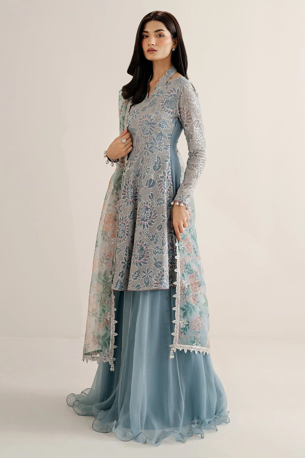 Woman wearing a traditional outfit with embroidered chiffon anarkali top and light blue palazzo pants on a plain background