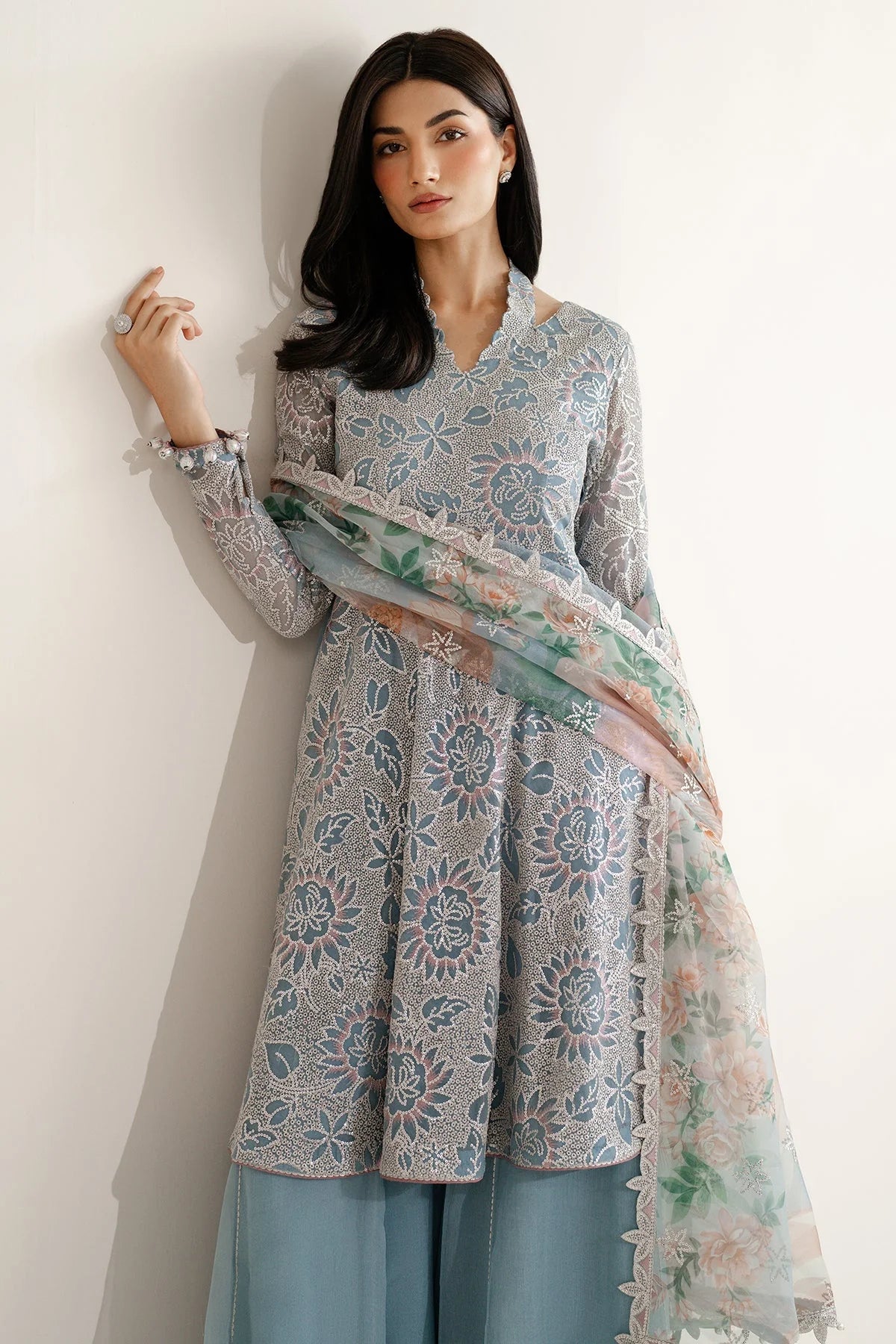 Woman wearing a traditional outfit with embroidered chiffon anarkali top and light blue palazzo pants on a plain background