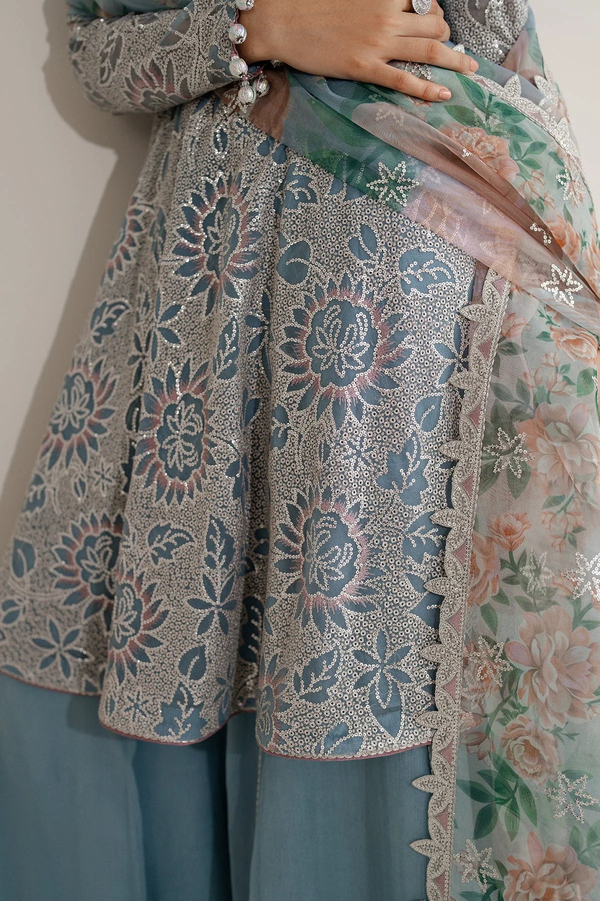 Woman wearing a traditional outfit with embroidered chiffon anarkali top and light blue palazzo pants on a plain background