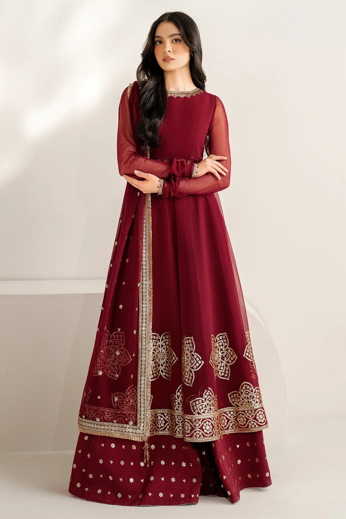 Woman wearing a maroon traditional outfit with gold embroidery on a white background