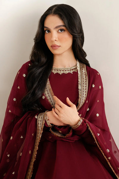 Woman wearing a long maroon anarkali dress with gold embroidery on a white backgroundWoman wearing a long maroon anarkali dress with gold embroidery on a white background