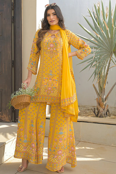 Woman in a yellow sharara suit traditional outfit with floral patterns standing outdoors.Woman in a yellow sharara suit traditional outfit with floral patterns standing outdoors.