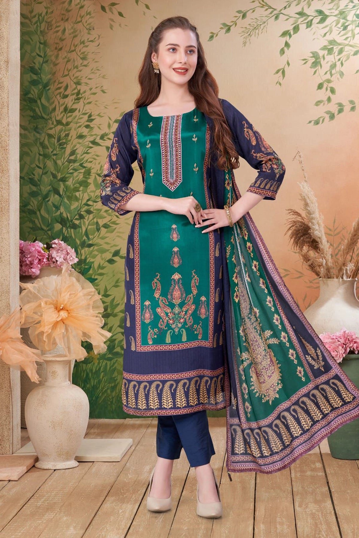 Woman wearing a green and blue embroidered traditional kurta pant style outfit with a floral background