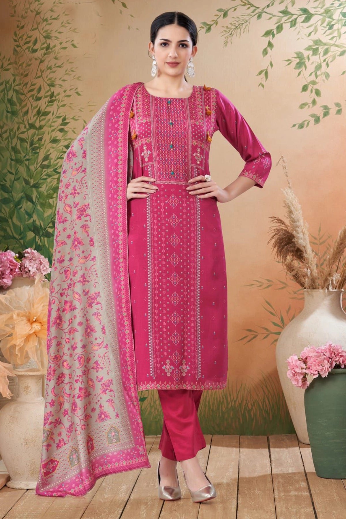 Woman wearing a pink traditional outfit with a floral dupatta against a decorative background.