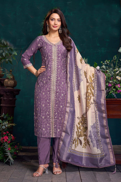Woman wearing a purple traditional outfit with a matching dupatta against a dark green background.