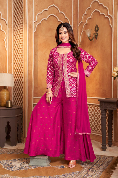 Woman in a pink traditional outfit with intricate patterns in a decorated room.