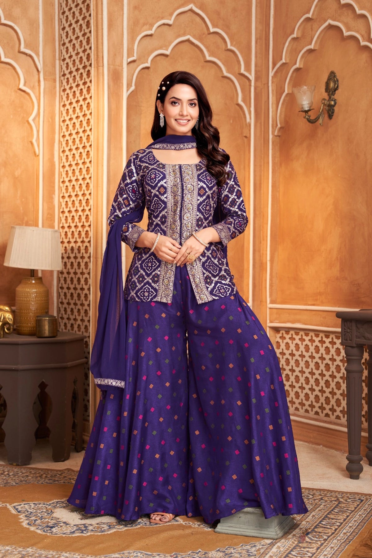 Woman in a traditional purple blue and purple outfit standing in an ornate room.