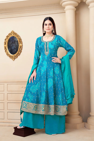 Woman in a teal traditional outfit standing in a decorated room.