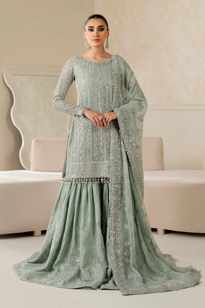 Woman wearing a light green traditional wedding sharara outfit with a matching dupatta in a room.