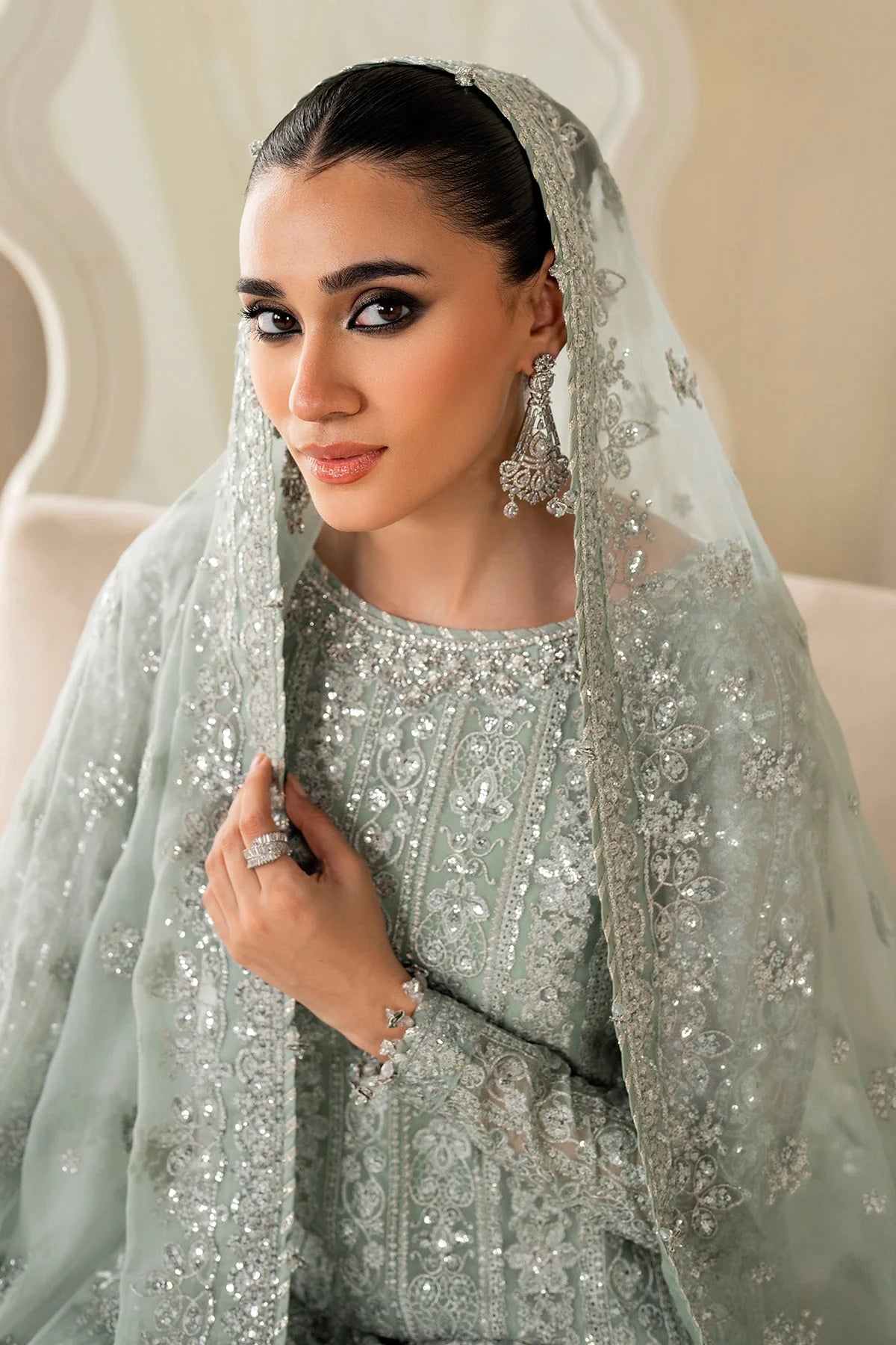 Woman wearing a light green traditional wedding sharara outfit with a matching dupatta in a room.