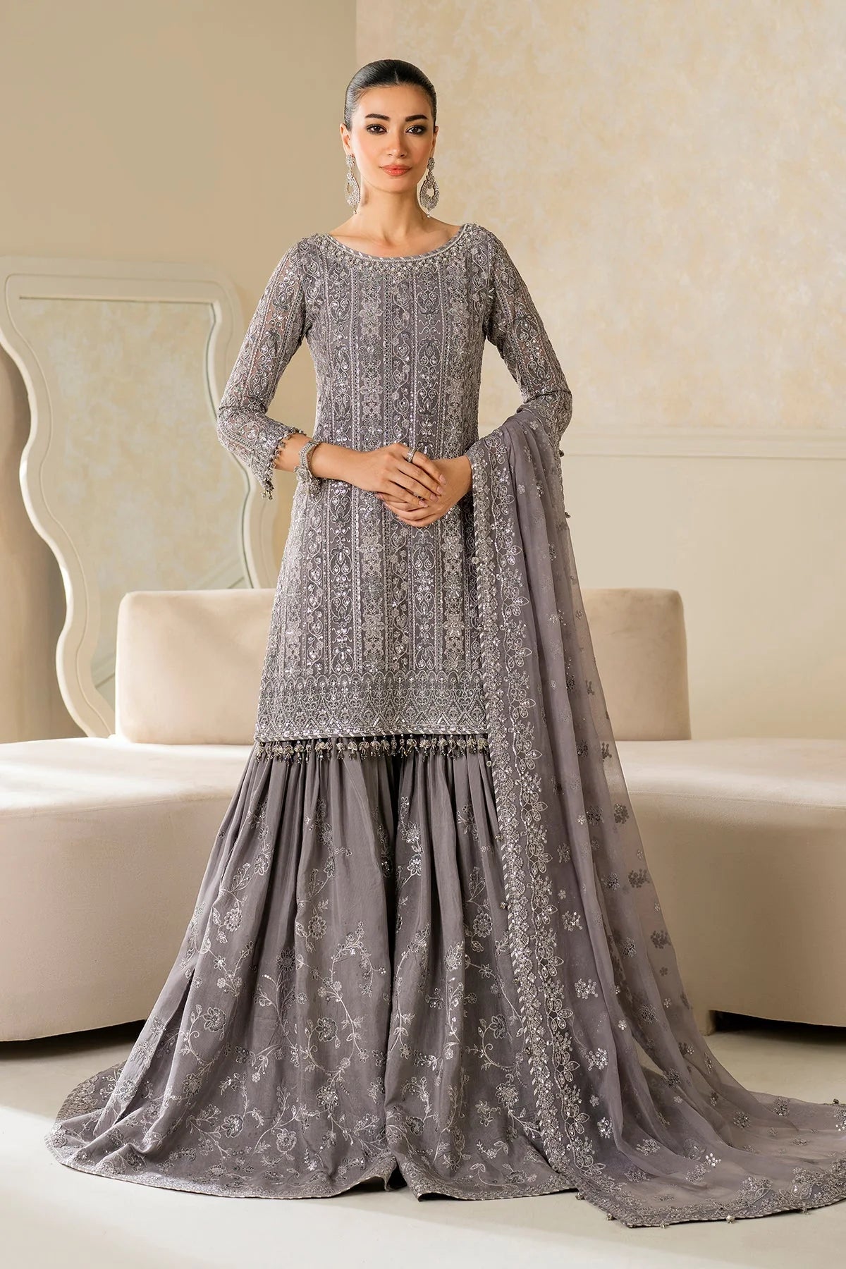 Woman wearing a gray embroidered traditional outfit with a matching dupatta in a room.