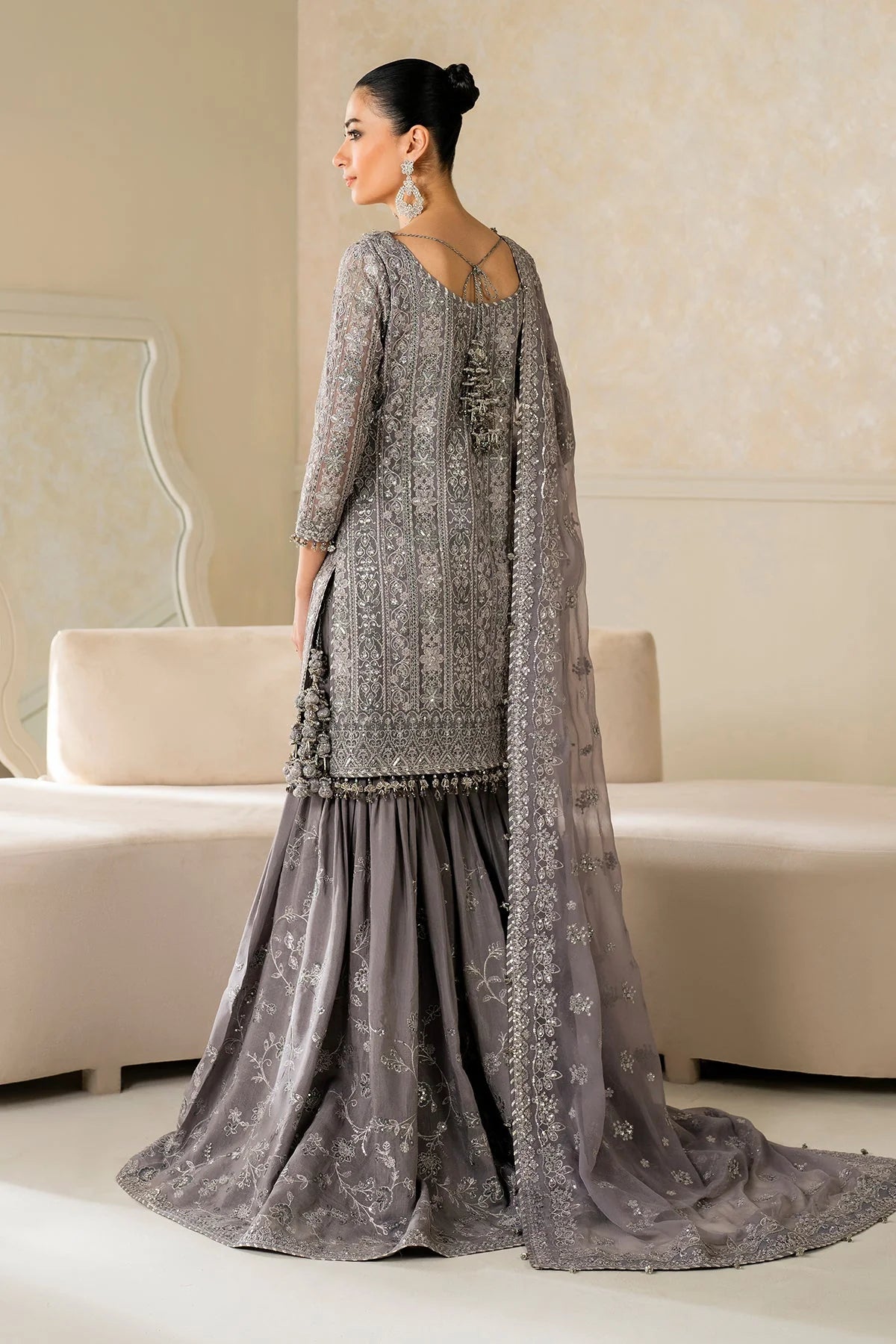 Woman in a gray traditional outfit standing in a room with beige walls and furniture.