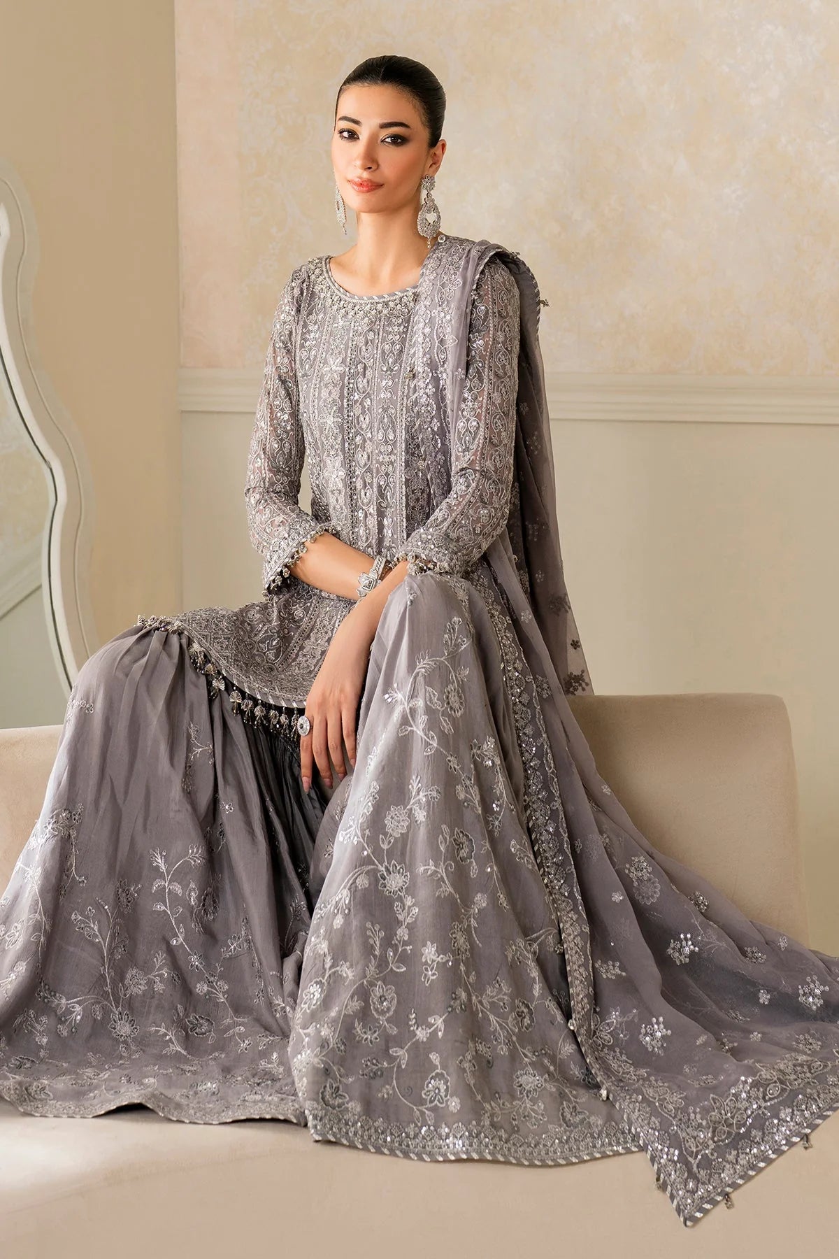 Woman wearing a gray traditional outfit with intricate designs in a well-lit room.