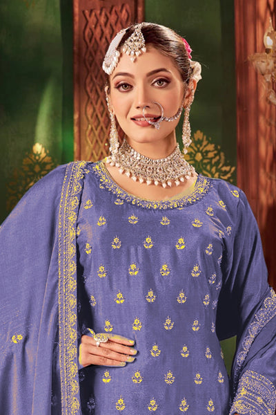 Woman in traditional blue embroidered sharara suit outfit with jewelry against a decorative backgroundWoman in traditional blue embroidered sharara suit outfit with jewelry against a decorative background