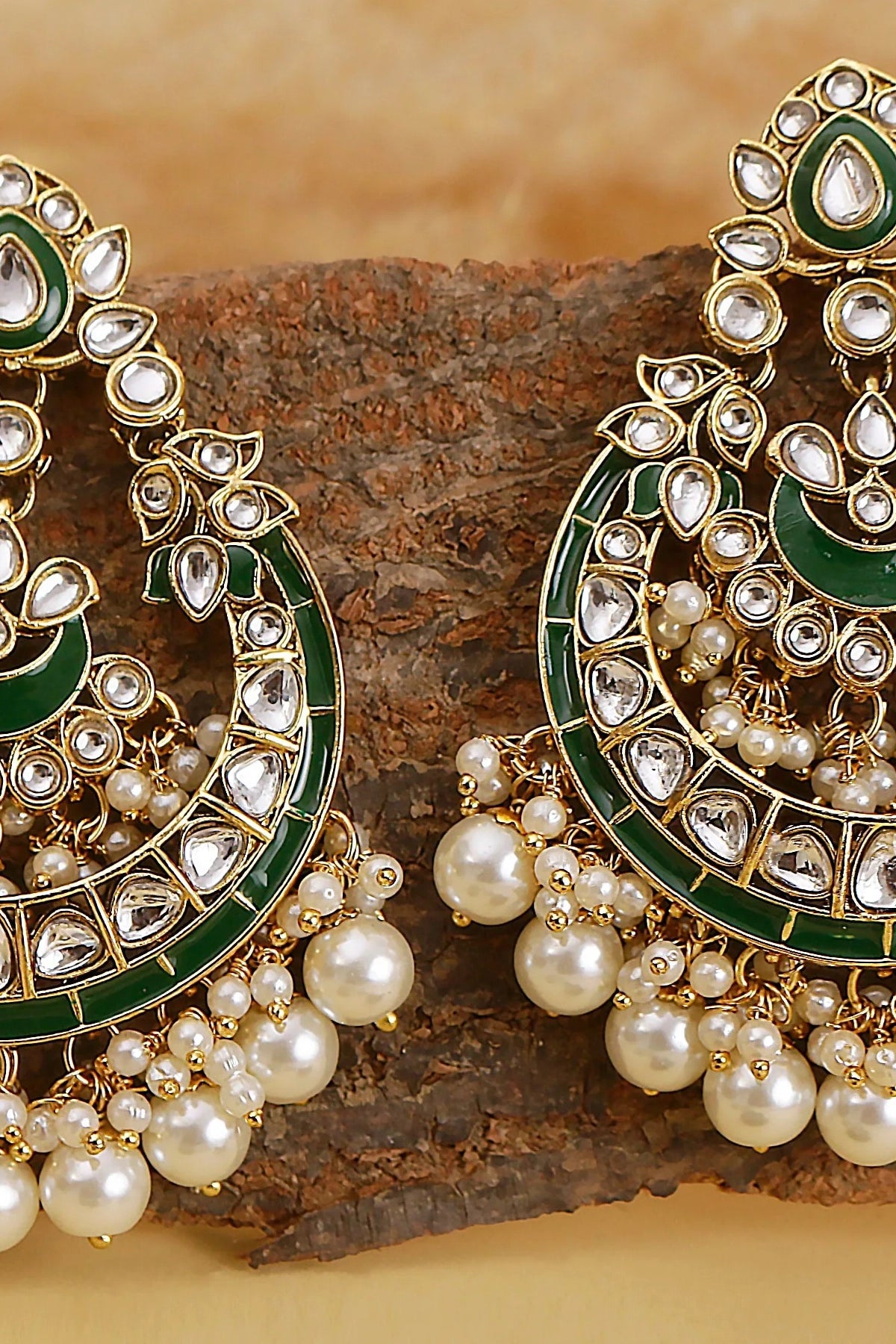 Ornate earrings with green and gold accents on a wooden surface