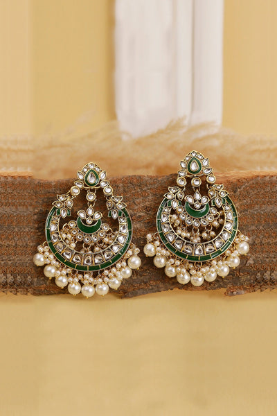 Ornate earrings with pearls and green accents on a wooden surface