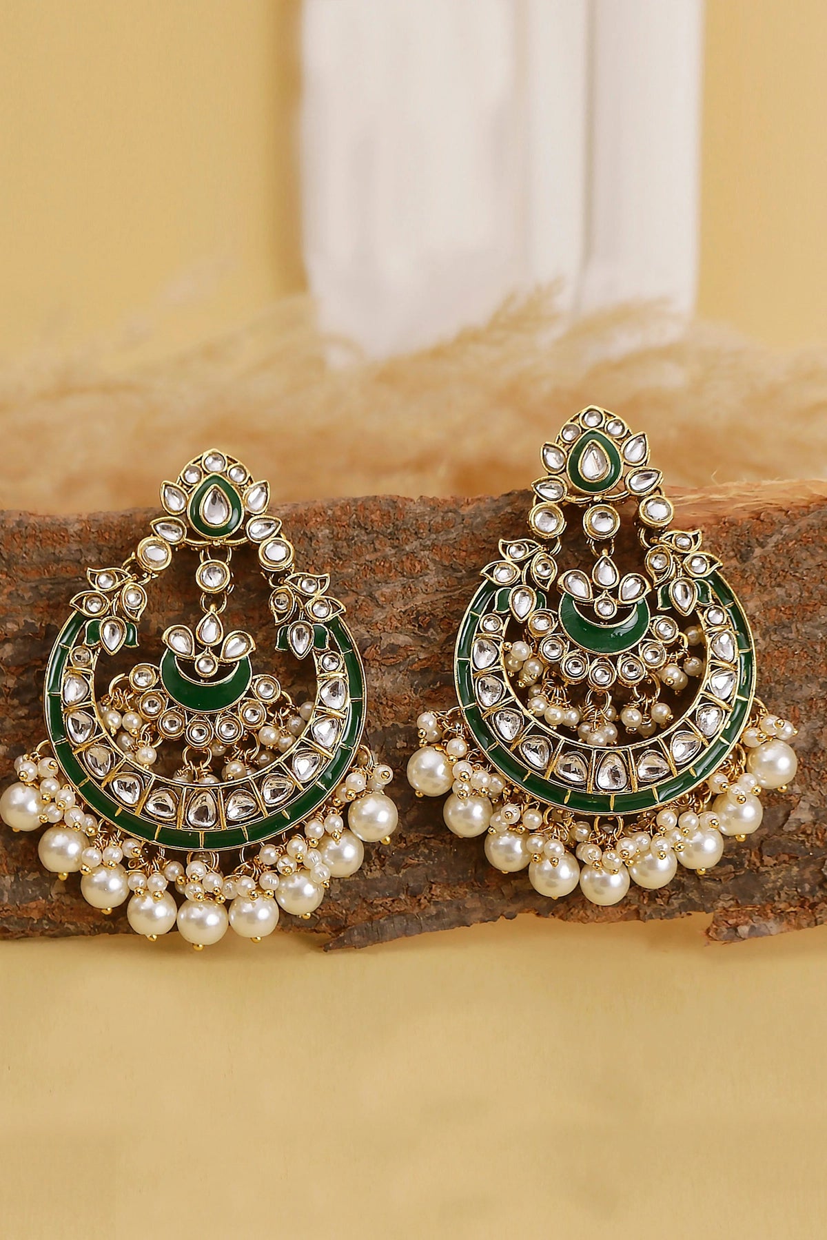 Pair of ornate earrings with green and gold details on a wooden surface.