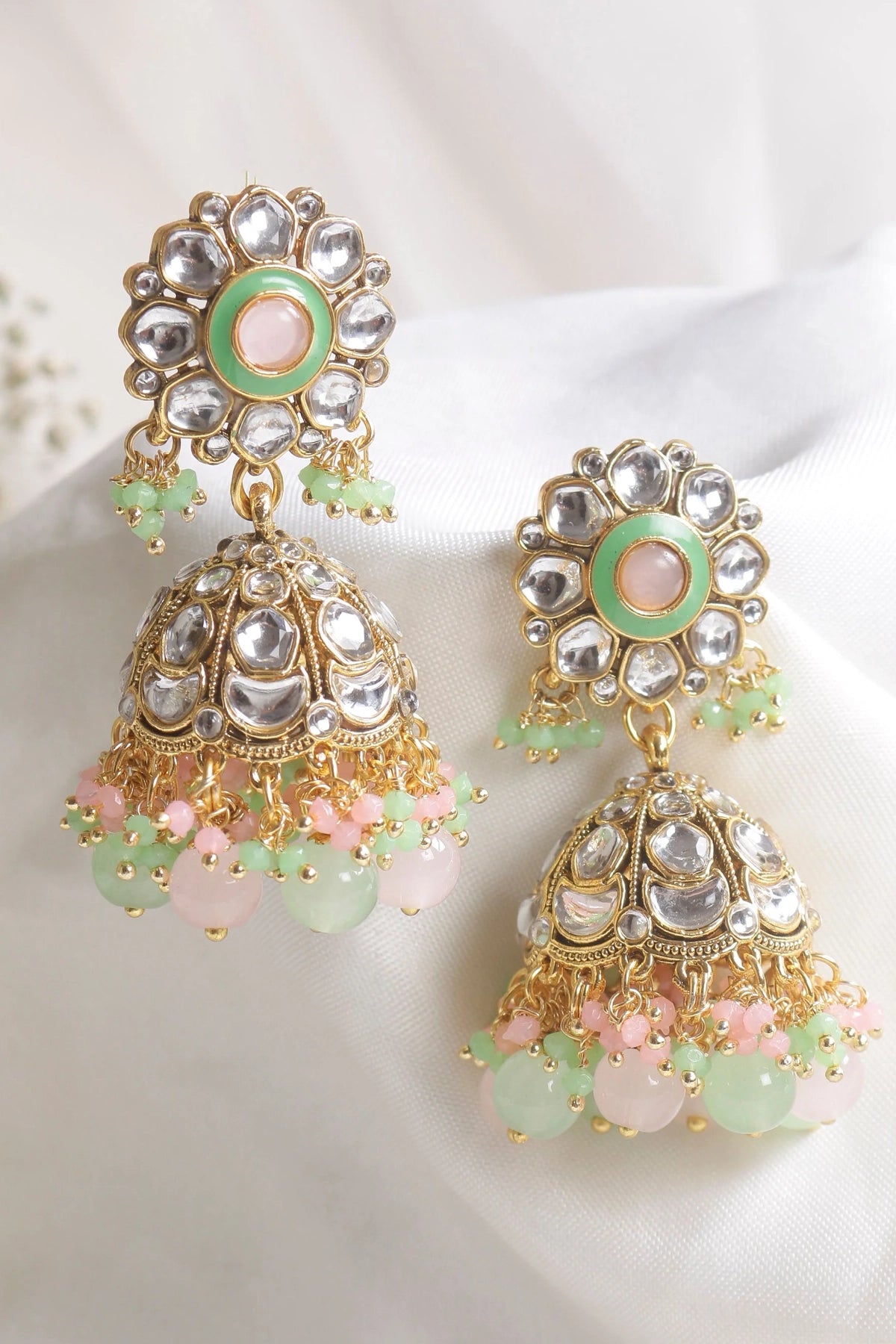 Ornate earrings with gold, green, and pink details on a white background