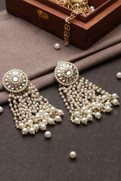 Pearl earrings with gold accents on a dark surface with a jewelry box in the background.