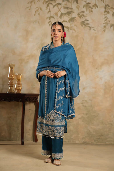 Woman in a blue traditional outfit with intricate patterns against a beige wall.Woman in a blue traditional outfit with intricate patterns against a beige wall.