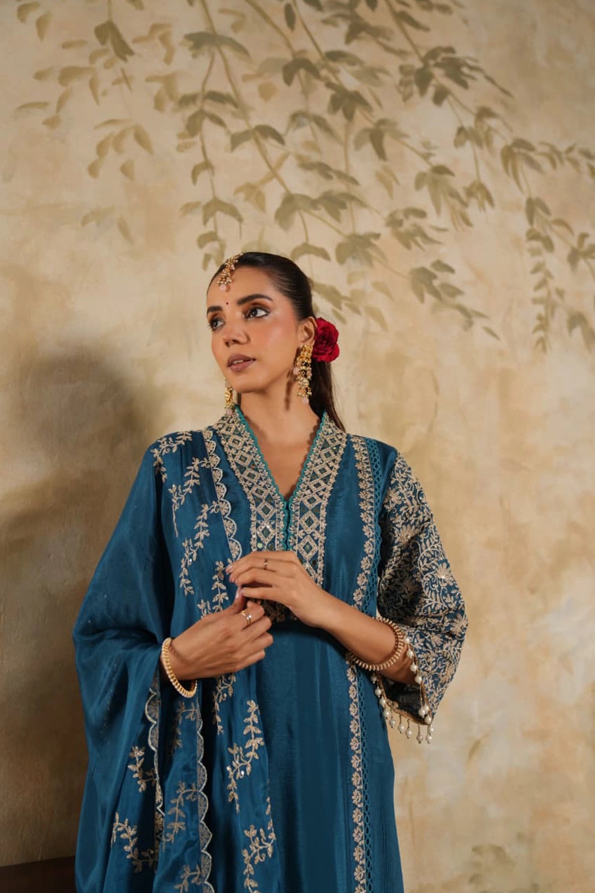 Woman in a blue embroidered outfit with a floral background