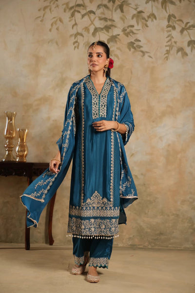 Woman in a blue embroidered traditional outfit standing against a beige wall.Woman in a blue embroidered traditional outfit standing against a beige wall.