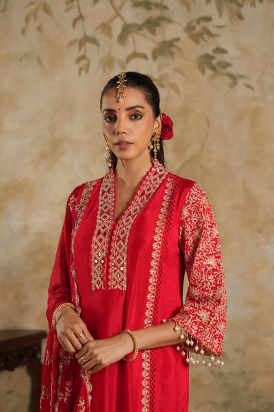 Woman in a rani pink traditional krta set outfit with gold embroidery against a beige wall.Woman in a rani pink traditional krta set outfit with gold embroidery against a beige wall.
