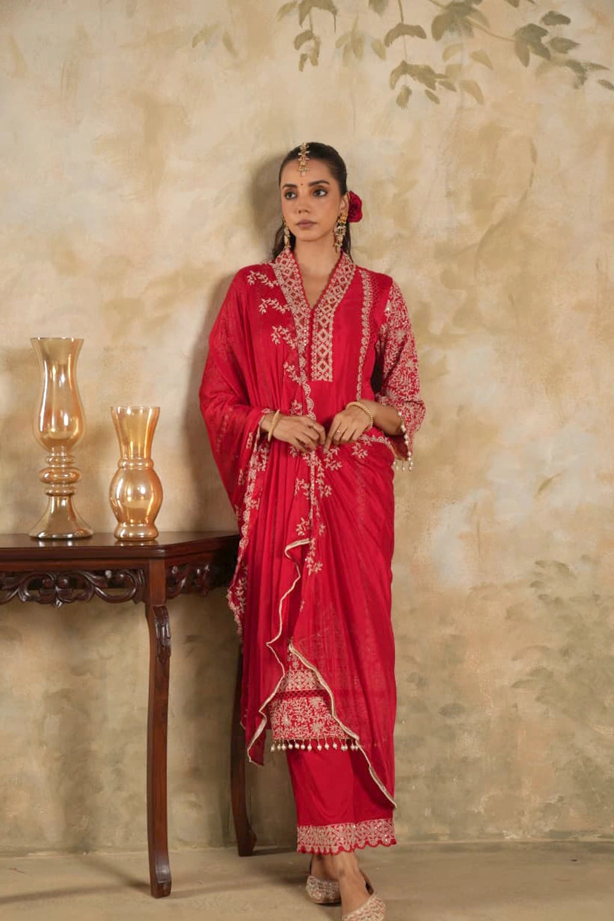 Woman in a rani pink traditional krta set outfit with gold embroidery against a beige wall.