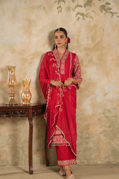 Woman in a rani pink traditional krta set outfit with gold embroidery against a beige wall.Woman in a rani pink traditional krta set outfit with gold embroidery against a beige wall.
