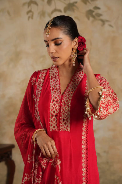 Woman in a rani pink traditional krta set outfit with gold embroidery against a beige wall.Woman in a rani pink traditional krta set outfit with gold embroidery against a beige wall.