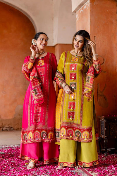 Two women in traditional embroidered dresses standing against an orange wall.Two women in traditional embroidered dresses standing against an orange wall.