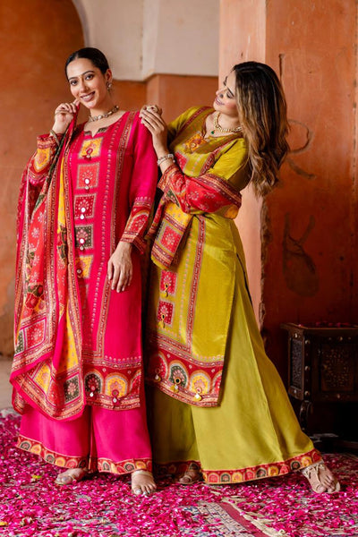 Two women in traditional pink and green sarees with intricate patterns standing against a warm-toned wall.Two women in traditional pink and green sarees with intricate patterns standing against a warm-toned wall.