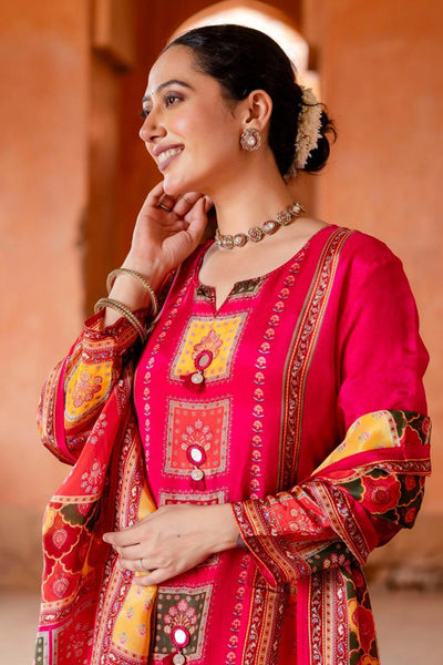 Woman wearing a traditional red and gold embroidered outfit with jewelry against an orange wall.Woman wearing a traditional red and gold embroidered outfit with jewelry against an orange wall.