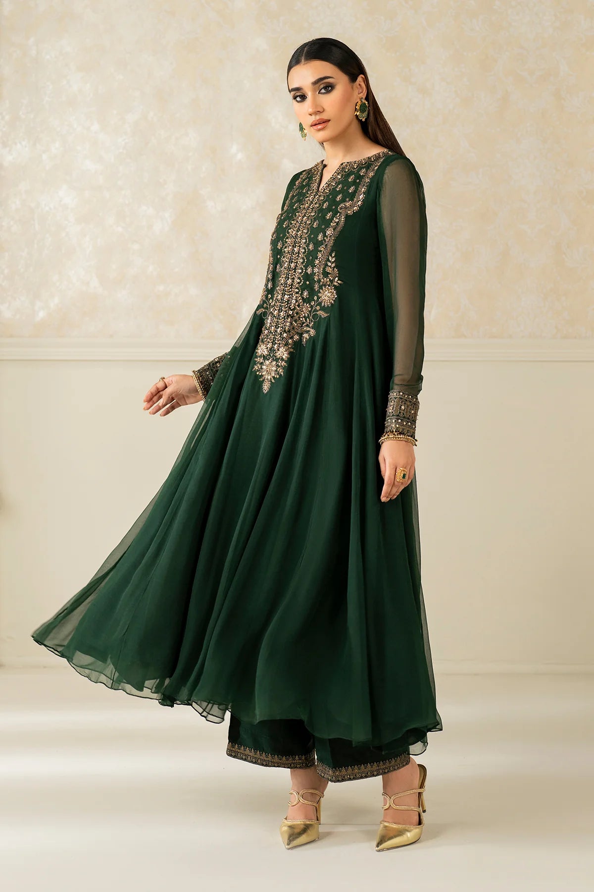 Woman wearing a green embroidered traditional anarkiali outfit with a chiffon dupatta against a neutral background