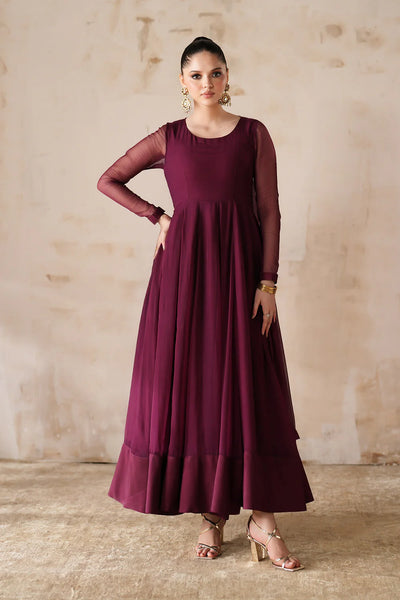 Woman wearing a burgundy chiffon anarkali dress with sheer sleeves against a beige wall.
