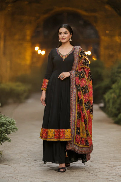 Woman in a black embroidered anarkali suit set with a colorful printed dupatta standing outdoors.