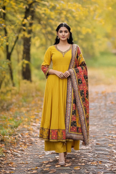 Woman in a yellow traditional outfit with a patterned dupatta standing in a forest during autumn.