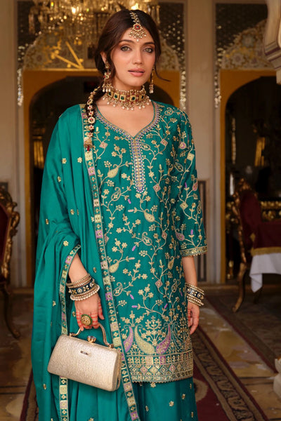 Woman in a teal traditional outfit with jewelry and a handbag in an ornate room.Woman in a teal traditional outfit with jewelry and a handbag in an ornate room.
