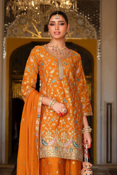Woman in an orange traditional sharara outfit with intricate patterns in a decorated room.Woman in an orange traditional sharara outfit with intricate patterns in a decorated room.